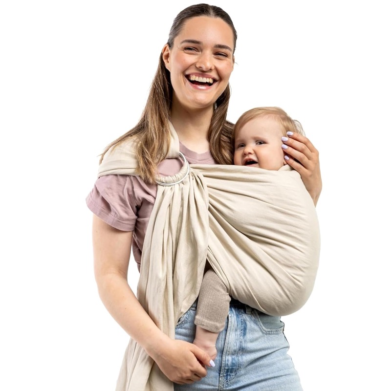woman wearing a cream boba ring sling over one shoulder with a laughing baby on her front