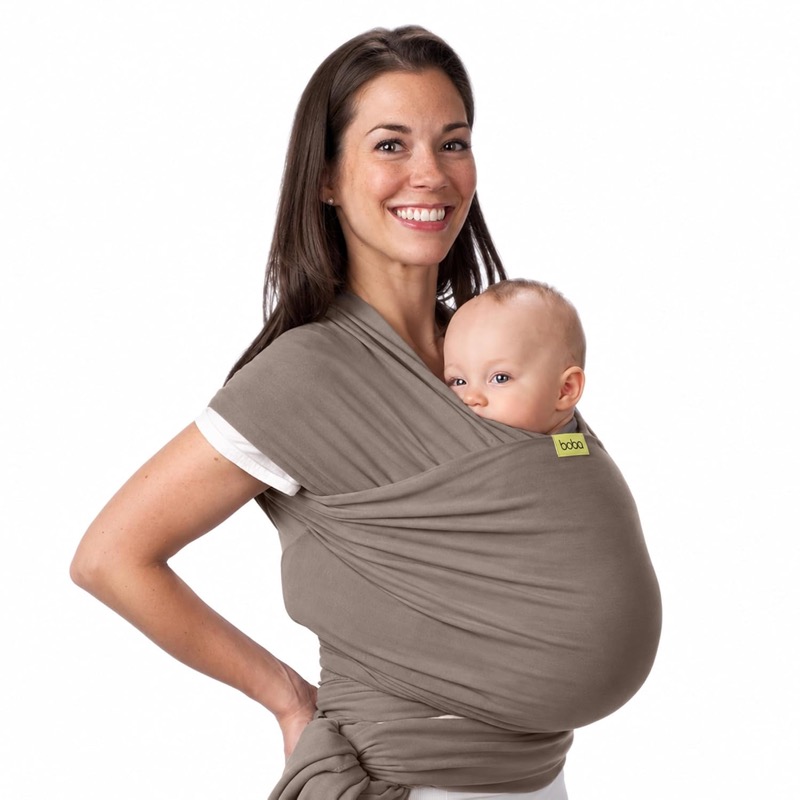 smiling woman wearing a taupe boba stretchy wrap with a baby held high on her chest