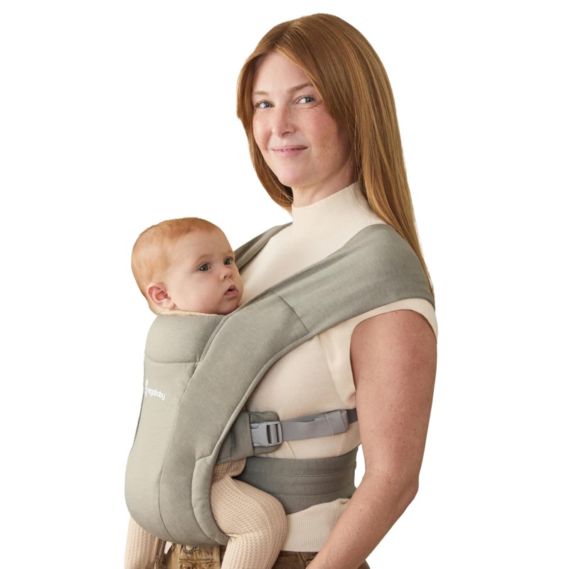 woman wearing a sage green ergobaby embrace knit carrier with a young baby facing her chest