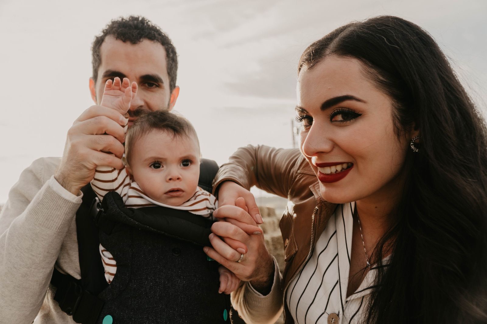 father wearing a baby in a dark front carrier with the baby's face uncovered, next to a smiling woman outdoors