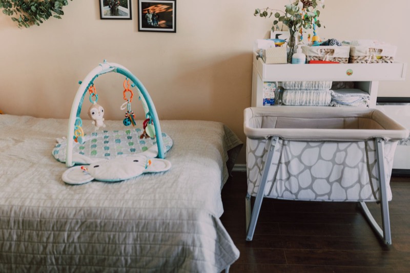 nursery with a mesh bassinet beside a changing table, a play mat on the floor and framed pictures on the wall