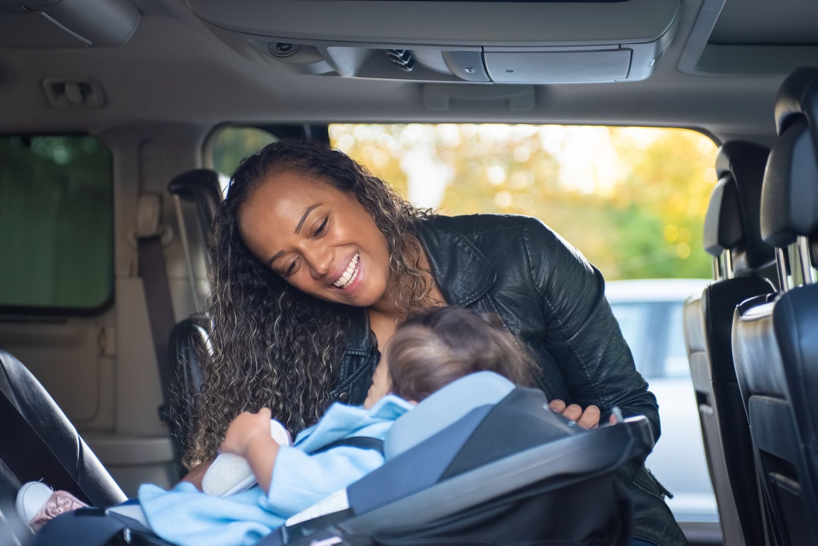 smiling mother leaning into a minivan to check on her baby in a rear-facing infant car seat