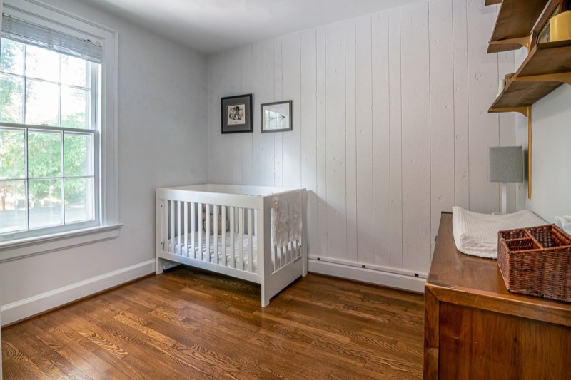 bright nursery with wooden floors, a window and a white crib with a bare mattress against the wall