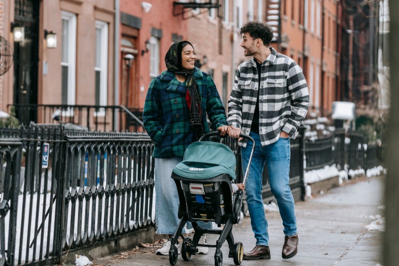 couple walking down a city sidewalk pushing a stroller with an infant car seat clicked onto the frame