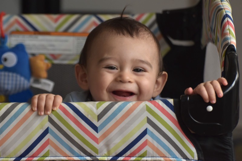 smiling baby peeking over the patterned side of a playpen