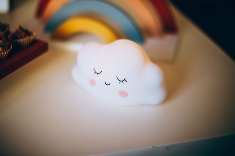 small cloud-shaped night light glowing softly in a dark room with a rainbow behind it