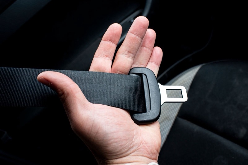 hand holding a black seat belt strap with its metal tongue in a dark car