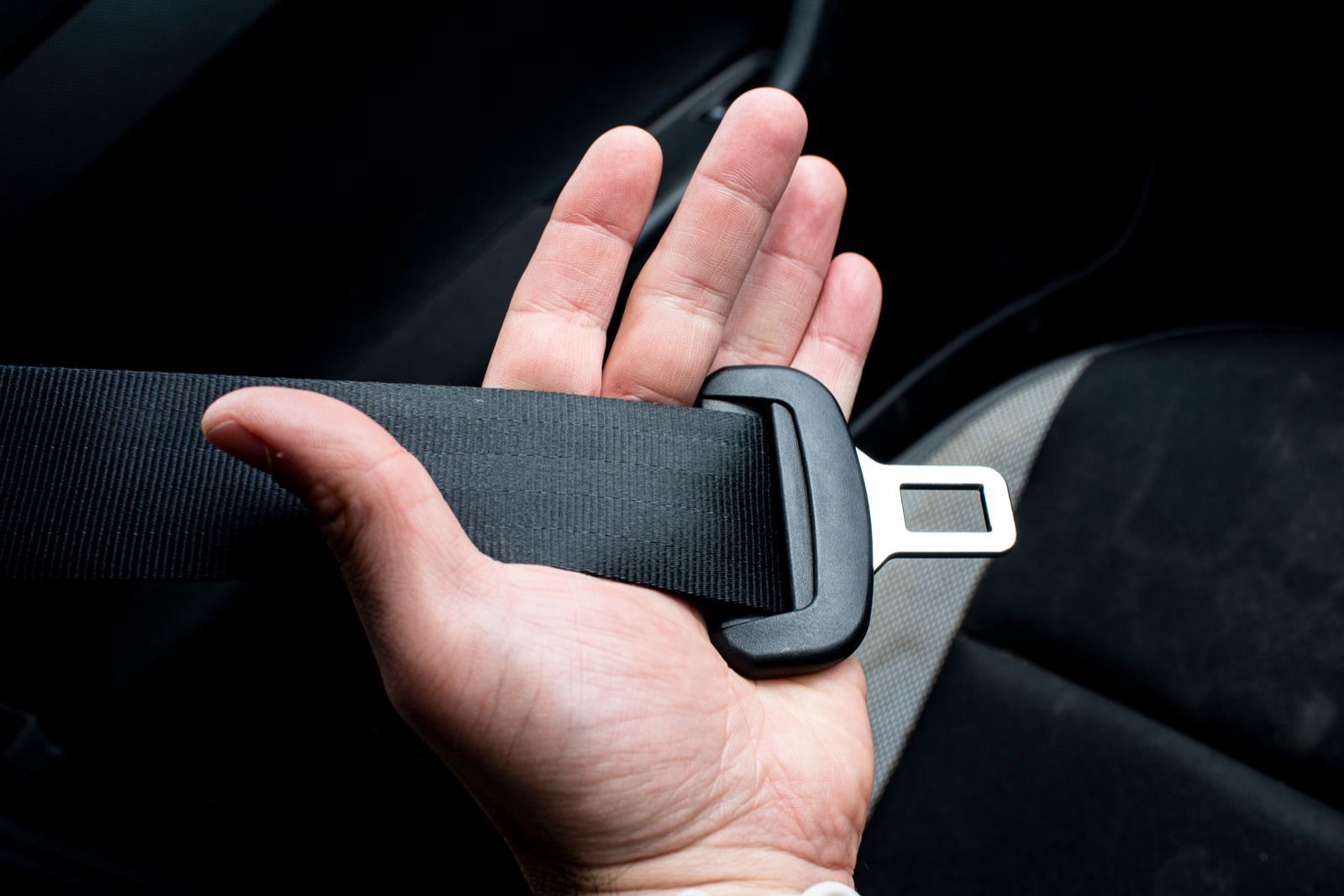 hand holding a black seat belt strap with its metal tongue in a dark car