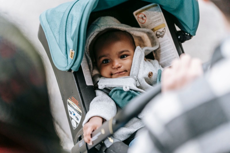 smiling baby in a teal infant car seat clicked onto a stroller, with a parent leaning in